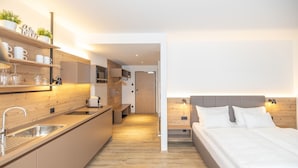 Een moderne hotelkamer met een kitchenette, een bed met witte lakens en een houten vloer.