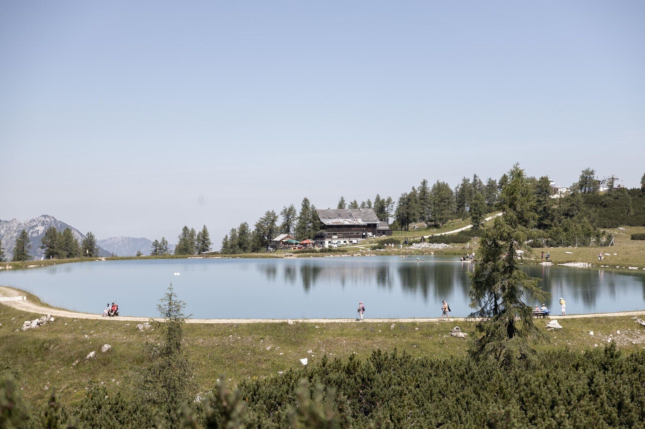 Un lago con un edificio al fondo, rodeado de árboles y montañas.