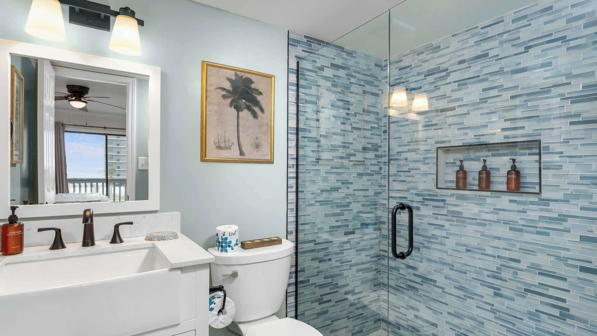 A bathroom with a glass shower enclosure, a white sink, and a framed picture on the wall.