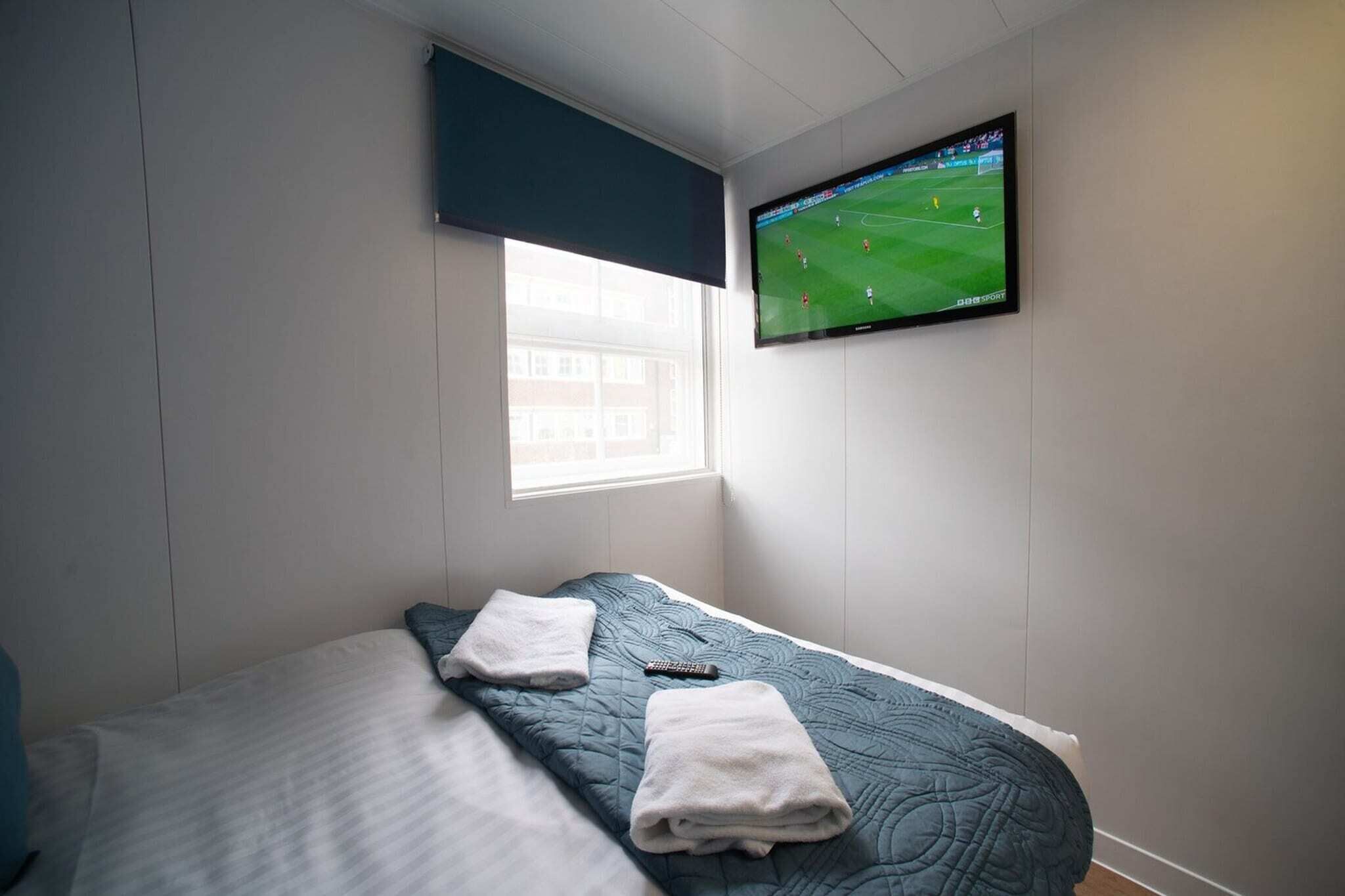 A hotel room with a bed, a television on the wall, and a window.