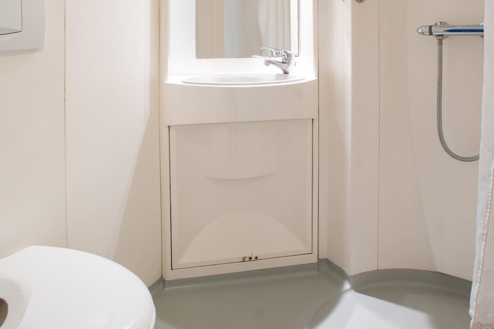 A bathroom with a white sink, a mirror above it, and a shower with a hose.