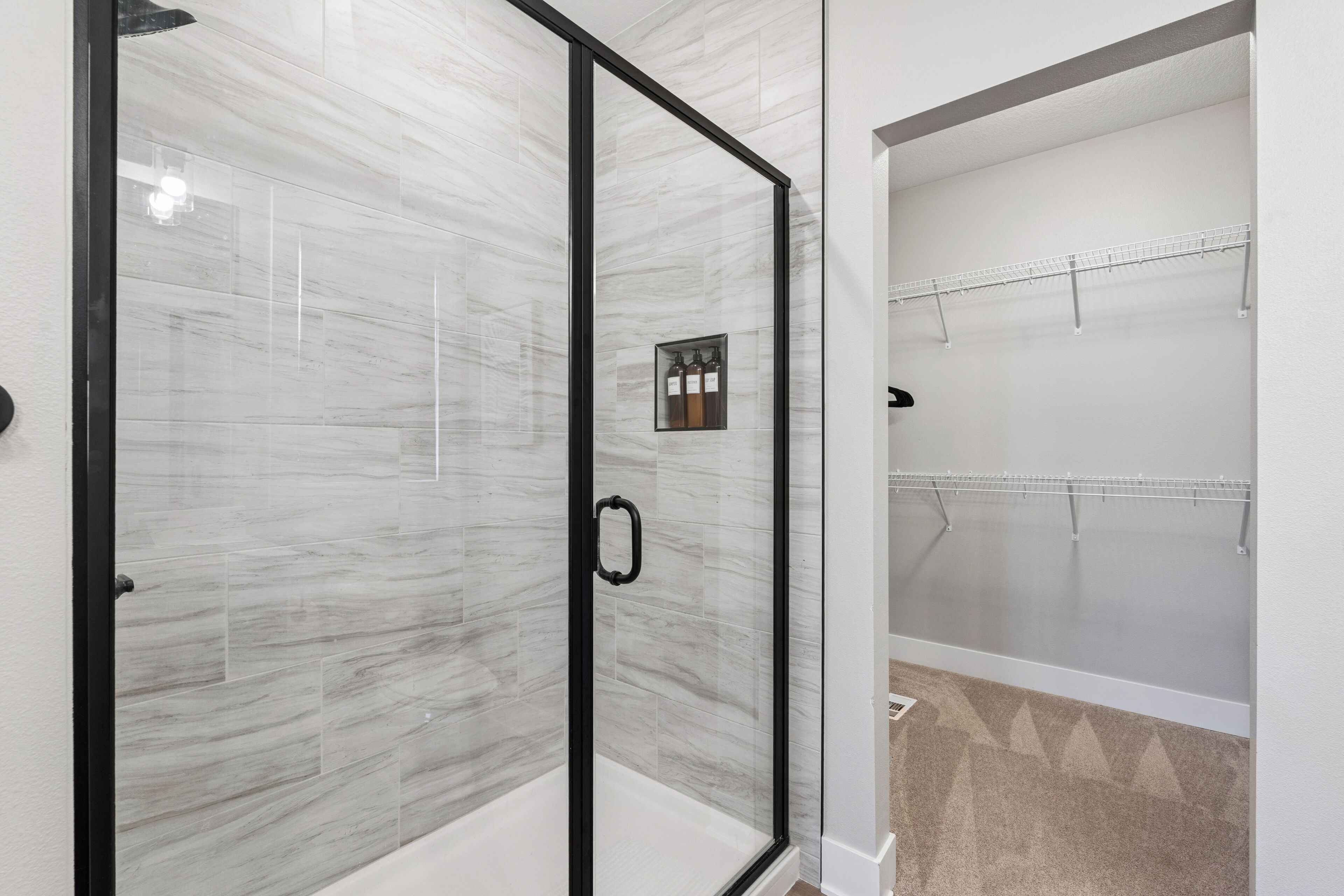Un baño con cabina de ducha de vidrio, pared con azulejos blancos y alfombra color beige.