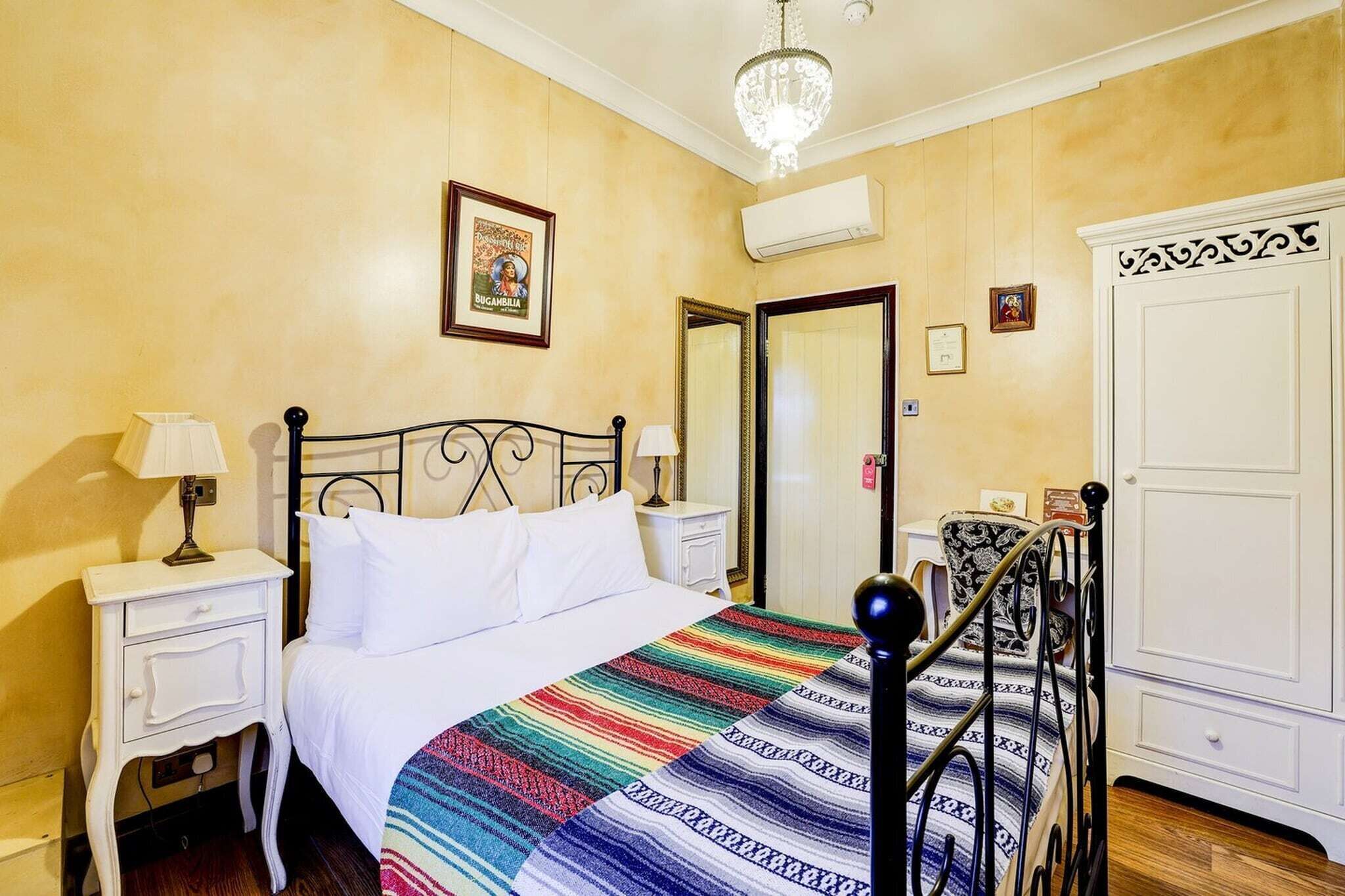 A hotel room with a bed, a nightstand with a lamp, a wardrobe, and a mirror.