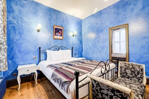 A bedroom with a bed, bedside table, chair, and a mirror.