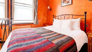 Una stanza con un letto, una finestra con tende, una lampada a muro e un quadro incorniciato.