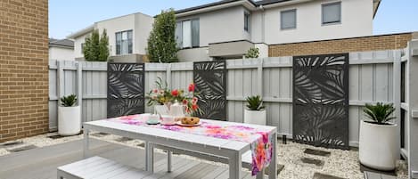 A patio with a white table and bench, surrounded by a wooden deck and a decorative fence.