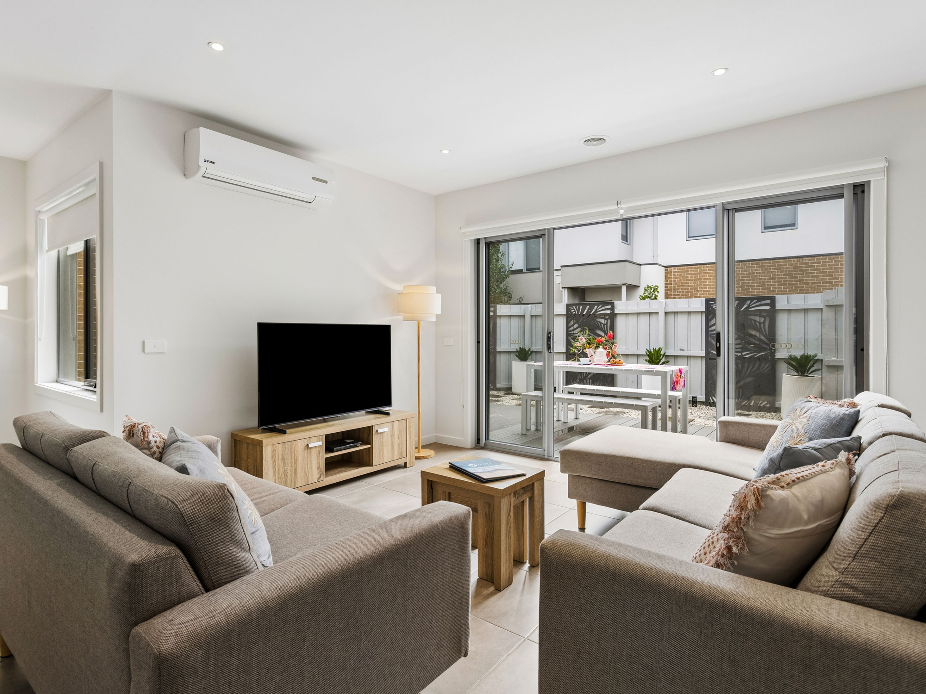 Ein modernes Wohnzimmer mit einem Flachbildfernseher, Sofas, einem Couchtisch und einer Schiebetür zu einer Außenpatio.