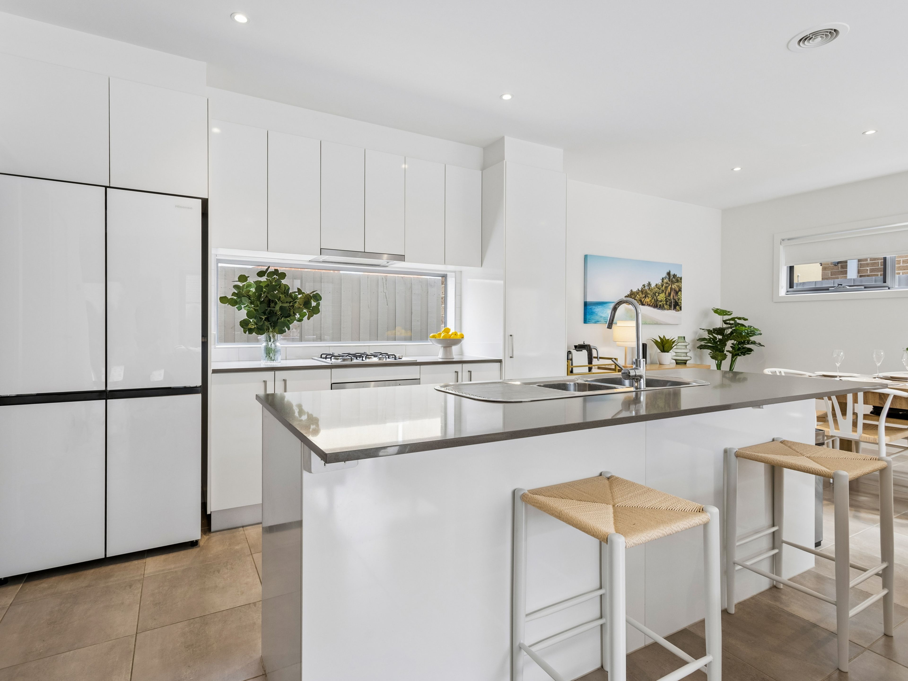 A modern kitchen with white cabinetry, a central island with stools, a gas stove, and a window with a plant.
