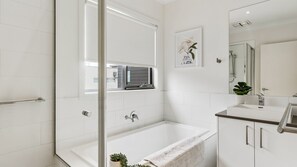 Et moderne badeværelse med badekar, vask, spejl og et vindue.