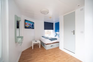 Un dormitorio con cama, una mesita, un espejo, un cuadro y una puerta.