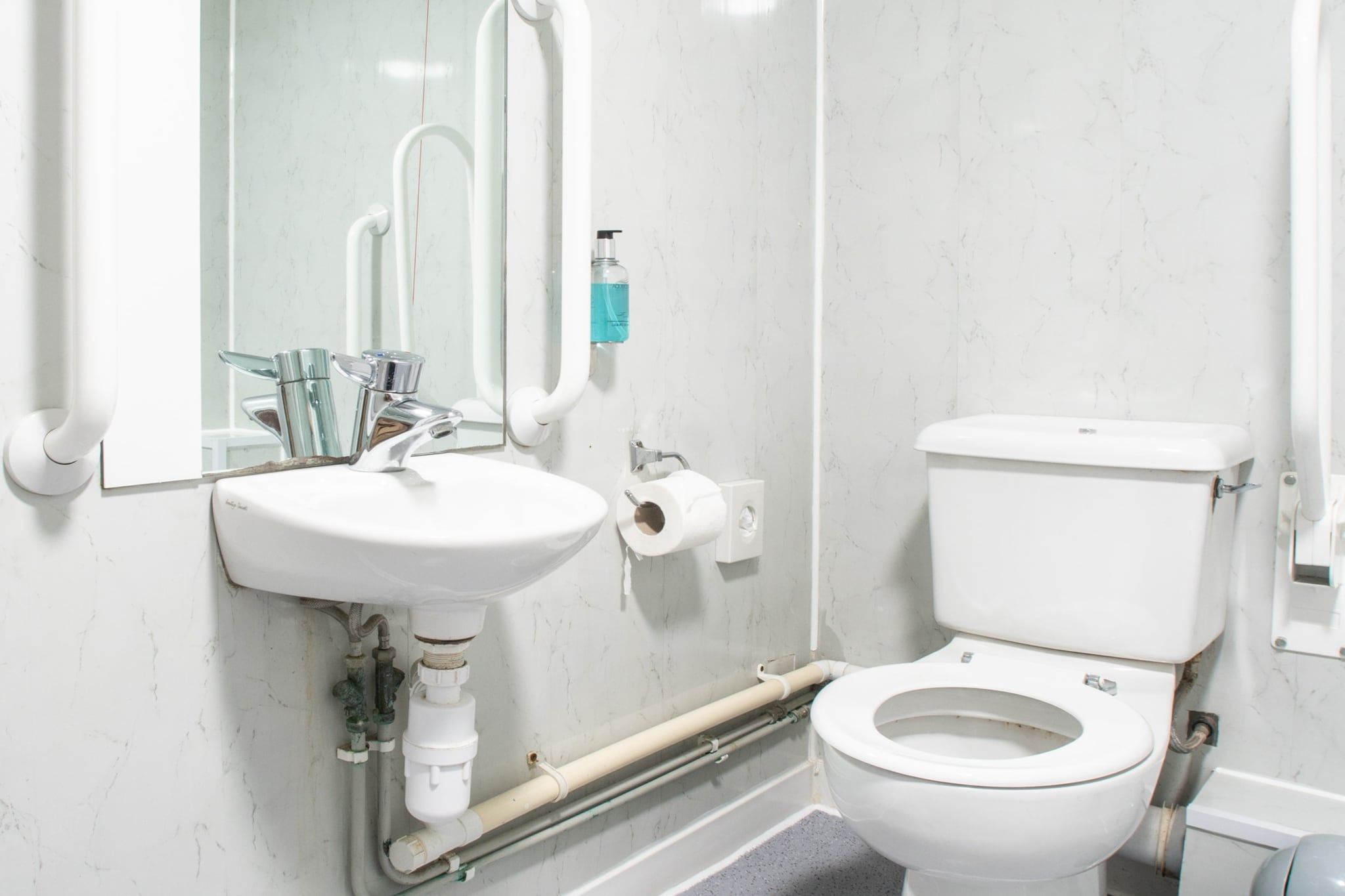 Een badkamer met een witte wasbak, een spiegel, een toilet en zichtbare leidingen.