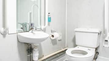 Een badkamer met een witte wasbak, een spiegel, een toilet en zichtbare leidingen.