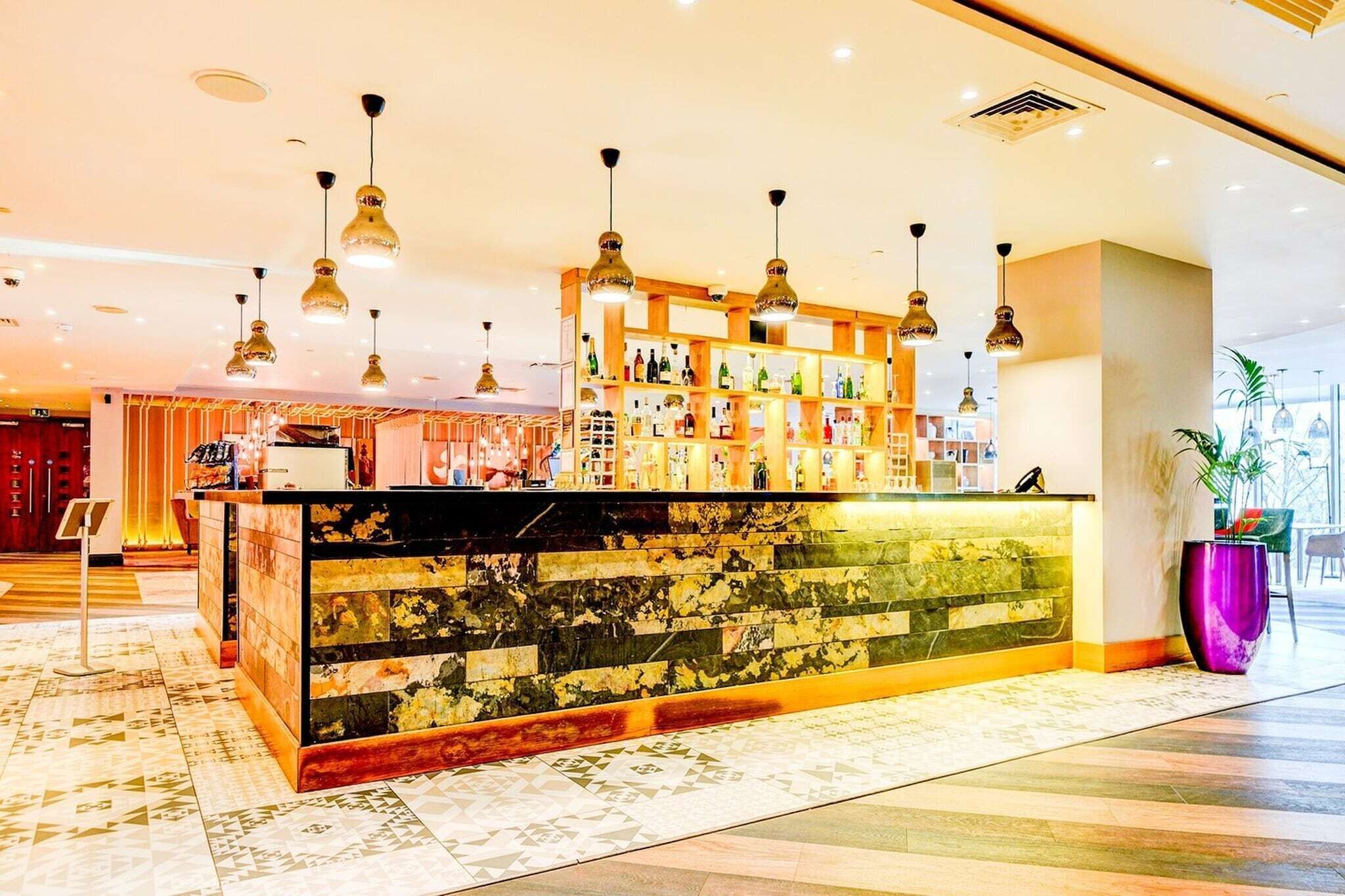 A bar area with a marble counter, hanging pendant lights, and a variety of bottles.