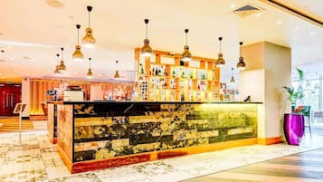 A bar area with a marble counter, hanging pendant lights, and a variety of bottles.