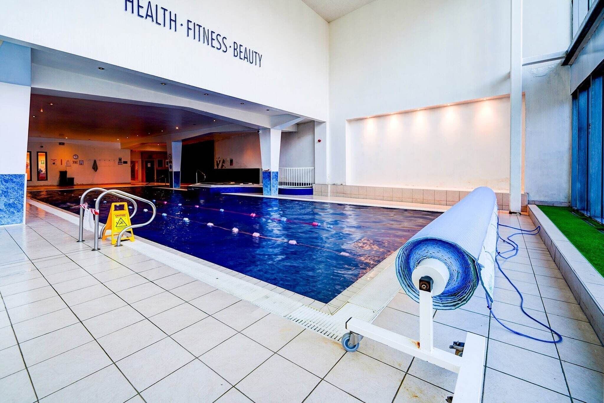 Ein Hallenbad mit Fliesenboden, einer Poolleiter und einem Schild, das auf einen Vorsichtsbereich hinweist.