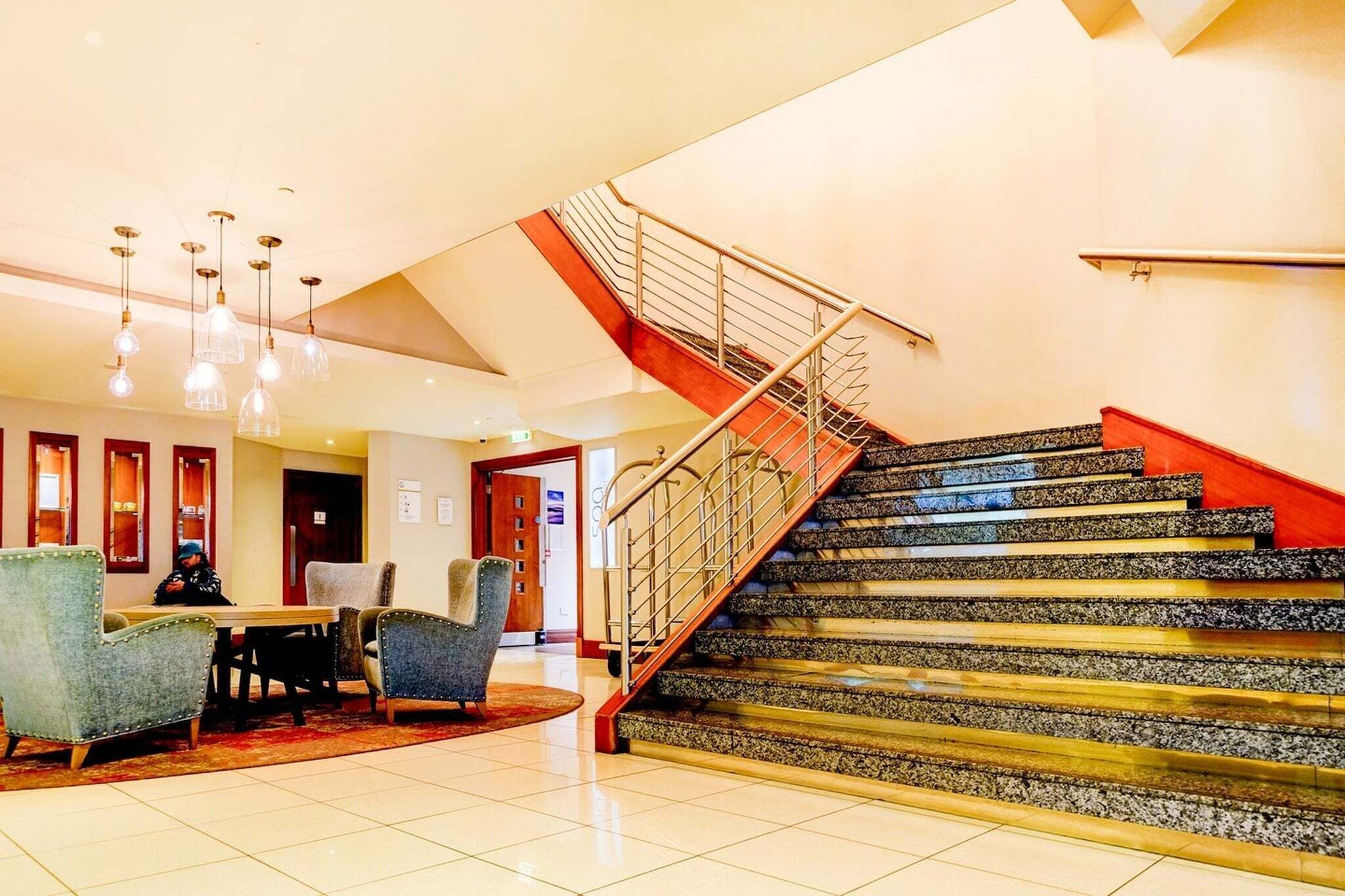 A hotel lobby with a staircase, seating area, and modern lighting.