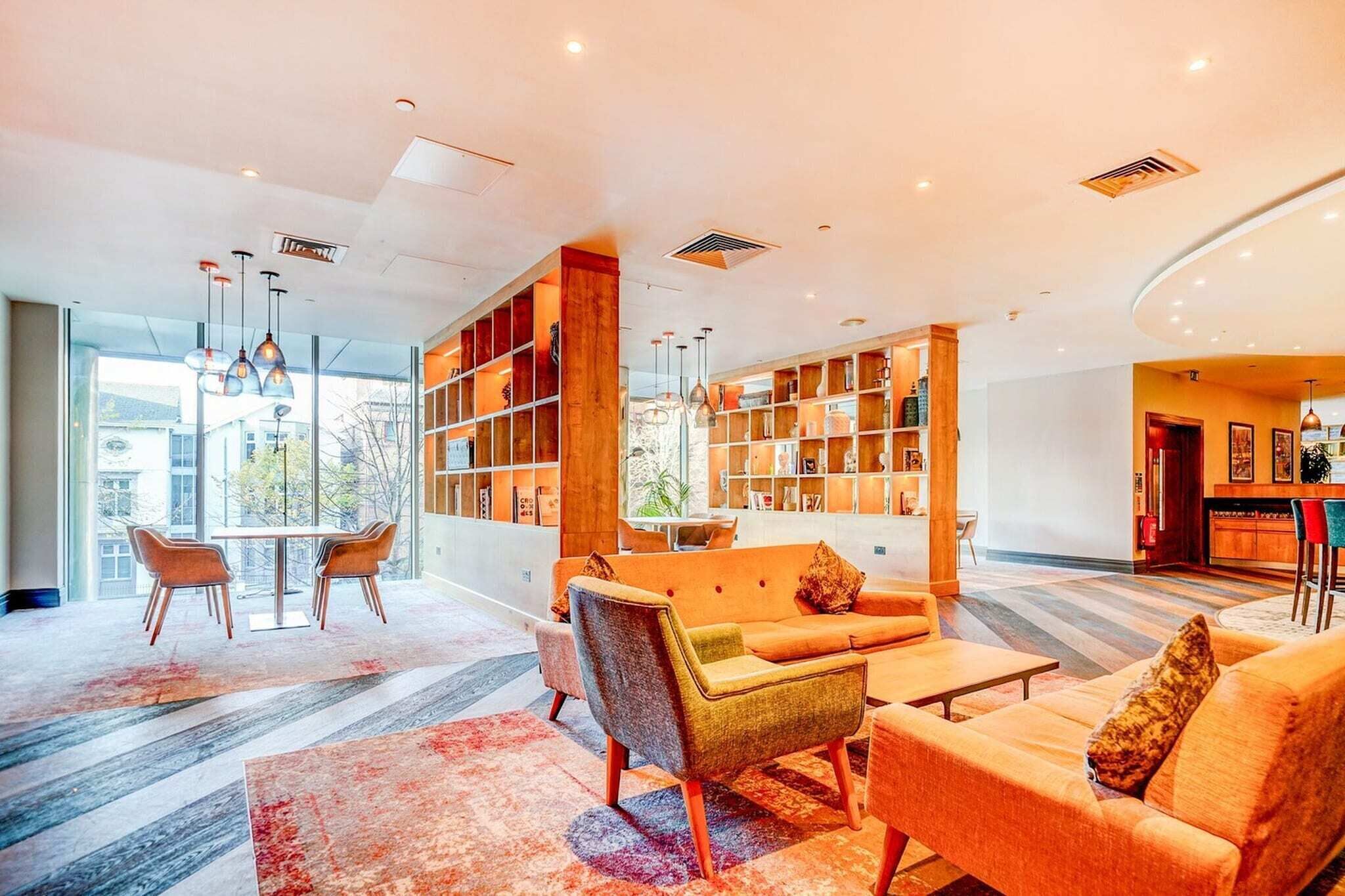 A modern lobby with a seating area, a bookshelf, and a view of the outside.