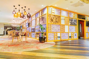 A hotel lobby with a central seating area, a large potted plant, and a decorative wall with images. - Holland House Hotel By Sunday Triple Room (Cardiff)