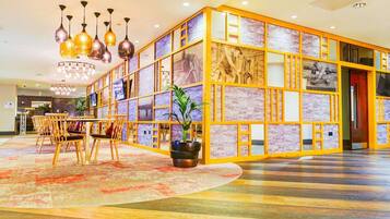 Een hotel lobby met een centrale zithoek, een grote potplant en een decoratieve muur met afbeeldingen.