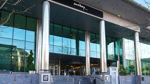 Moderni hotellin sisäänkäynti, jossa on suuret lasi-ikkunat, portaikko, joka johtaa aulaan, ja selkeästi näkyvä kyltti, jossa lukee »Sunday Hotel».