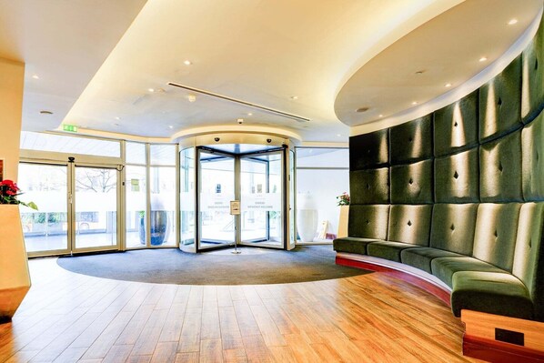 A lobby with a curved wooden floor, a green upholstered seating area, and a glass revolving door. - Privilege Room with Panoramic Views across thecity (Cardiff)