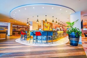 A bar area with a curved counter, multiple hanging pendant lights, and a large potted plant.