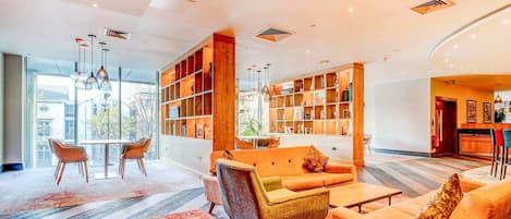 A modern lobby with a seating area, a bookshelf, and a view of the outside.