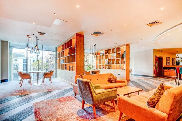 Een moderne lobby met een zithoek, een boekenkast en uitzicht op buiten.