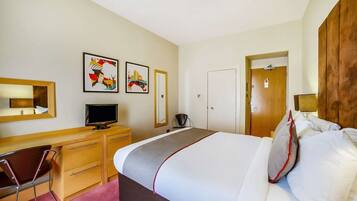 A hotel room with a bed, a desk with a computer, a chair, a television, and artwork on the walls.