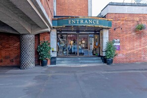A brick building with a sign reading 'ENTRANCE' above the door. There are two potted plants on either side of the entrance.