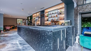 Un espace bar doté d’un comptoir en marbre, d’étagères remplies de bouteilles et d’un coin salon avec des chaises.