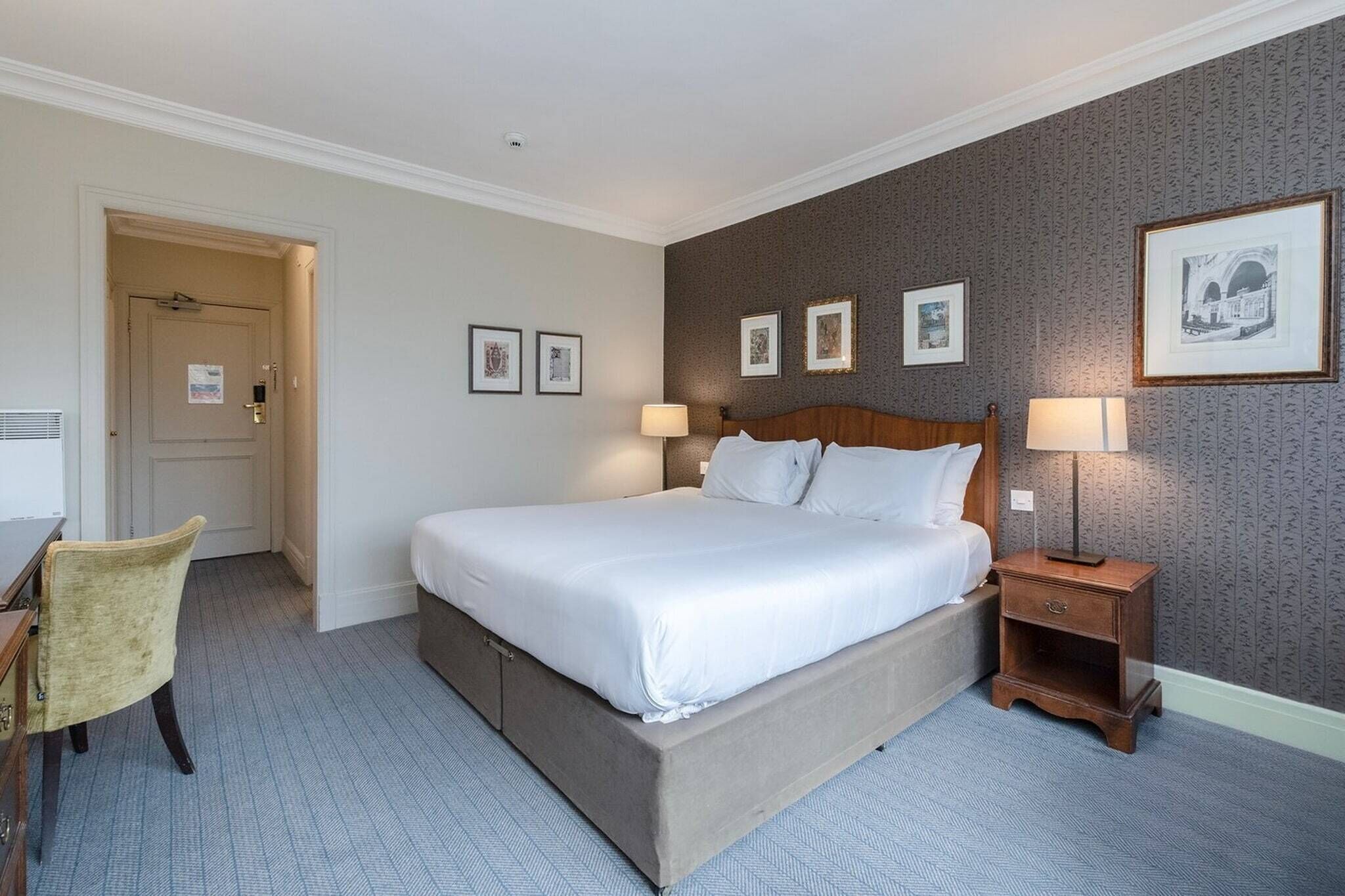 Ein Hotelzimmer mit einem Bett, Nachttischen, einem Sessel und gerahmten Bildern an der Wand.