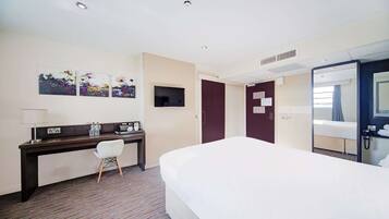 A hotel room with a bed, desk, chair, TV, and a bathroom mirror.