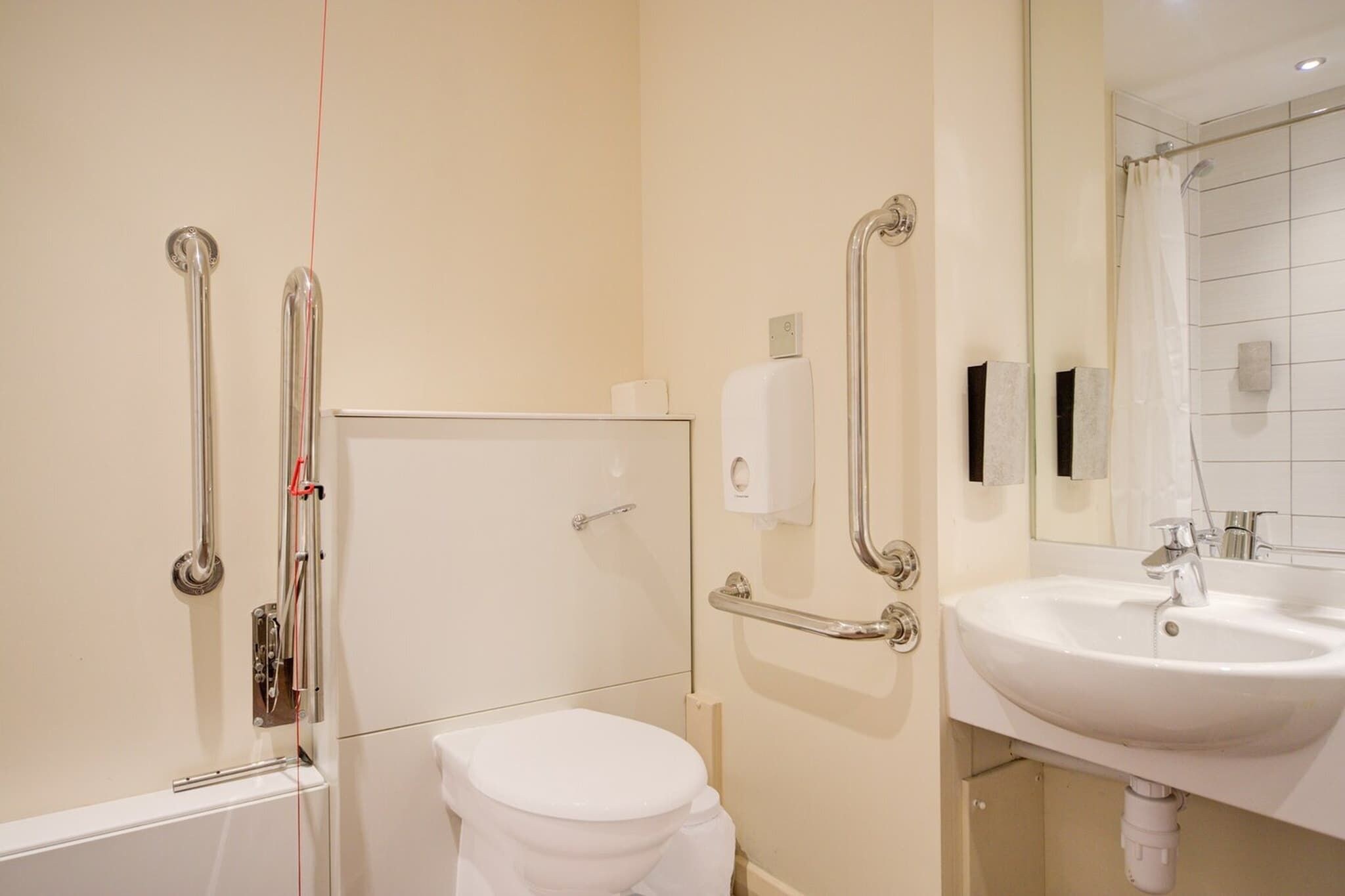 A bathroom with a white toilet, a sink, and a shower area with grab bars.