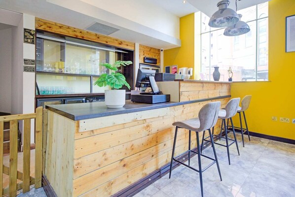 A bar area with a wooden counter, bar stools, a potted plant, and a window with a view.
