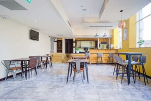 Un restaurante con zona de bar, varias mesas y sillas, una cocina al fondo y un ventanal grande.
