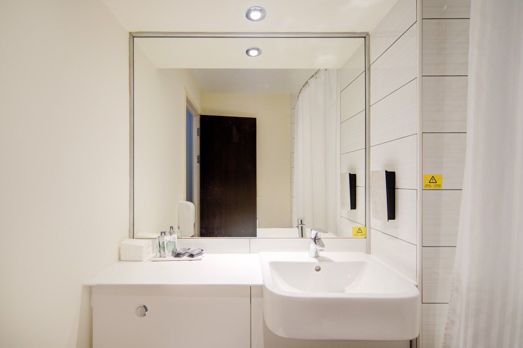 A modern bathroom with a double sink, a mirror, and a door leading to another room.