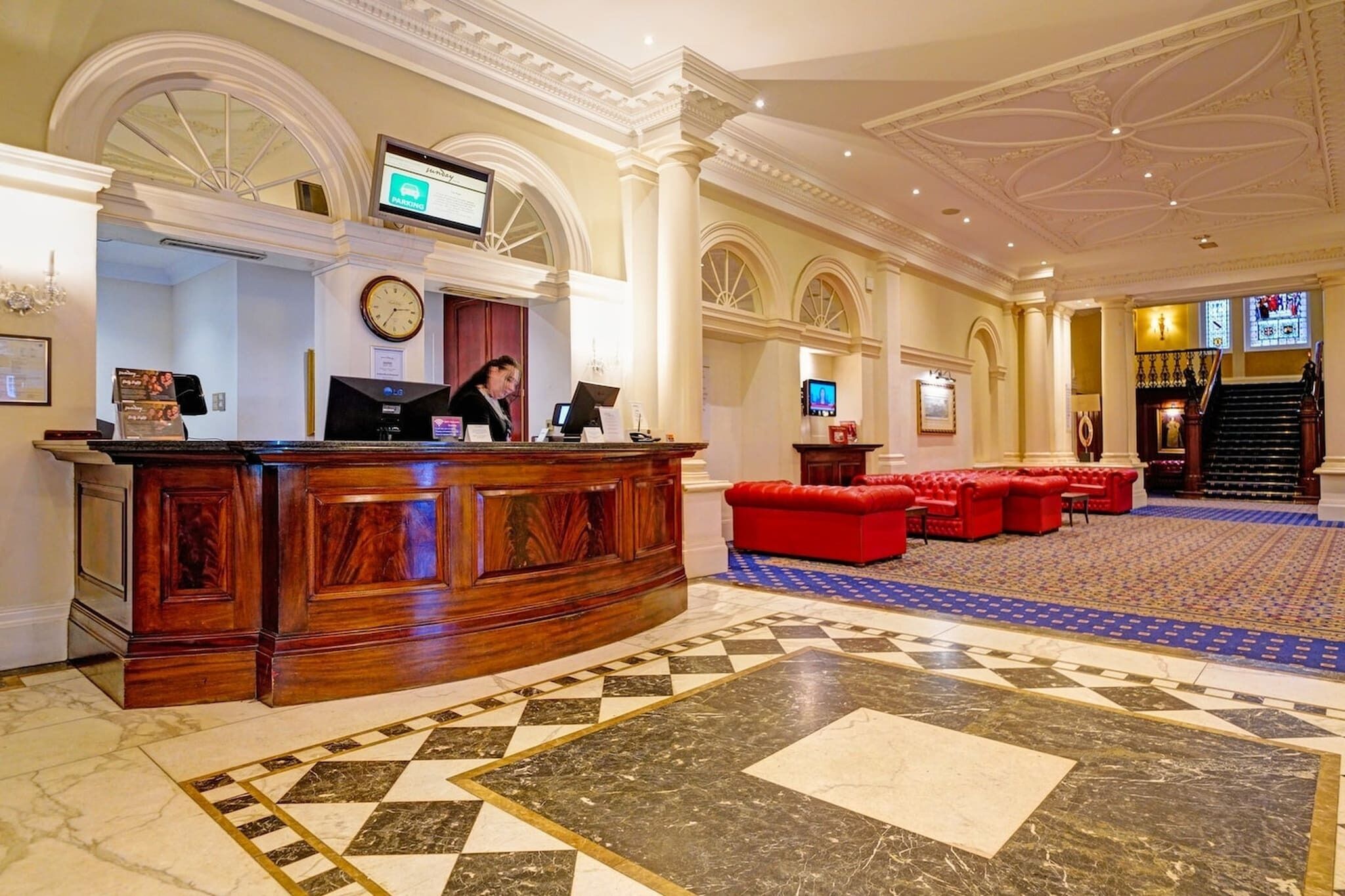 A lobby with a reception desk, a clock, a television, and a staircase.