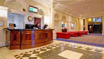A lobby with a reception desk, a clock, a television, and a staircase.