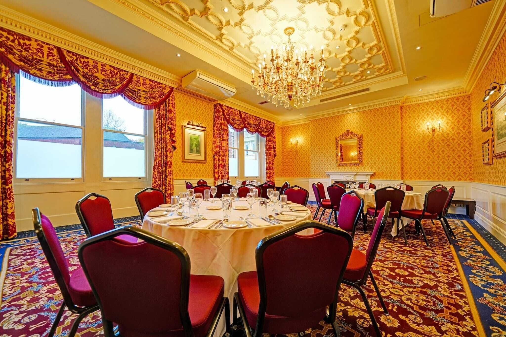 A conference room with round tables, red chairs, a chandelier, and patterned wallpaper.