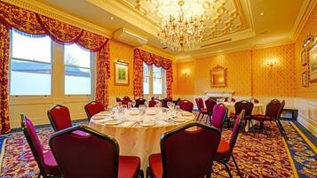 A conference room with round tables, red chairs, a chandelier, and patterned wallpaper.