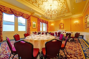 A conference room with round tables, red chairs, a chandelier, and patterned wallpaper. - Exeter Rougemont by Sunday - Privilege King Room (Exeter)