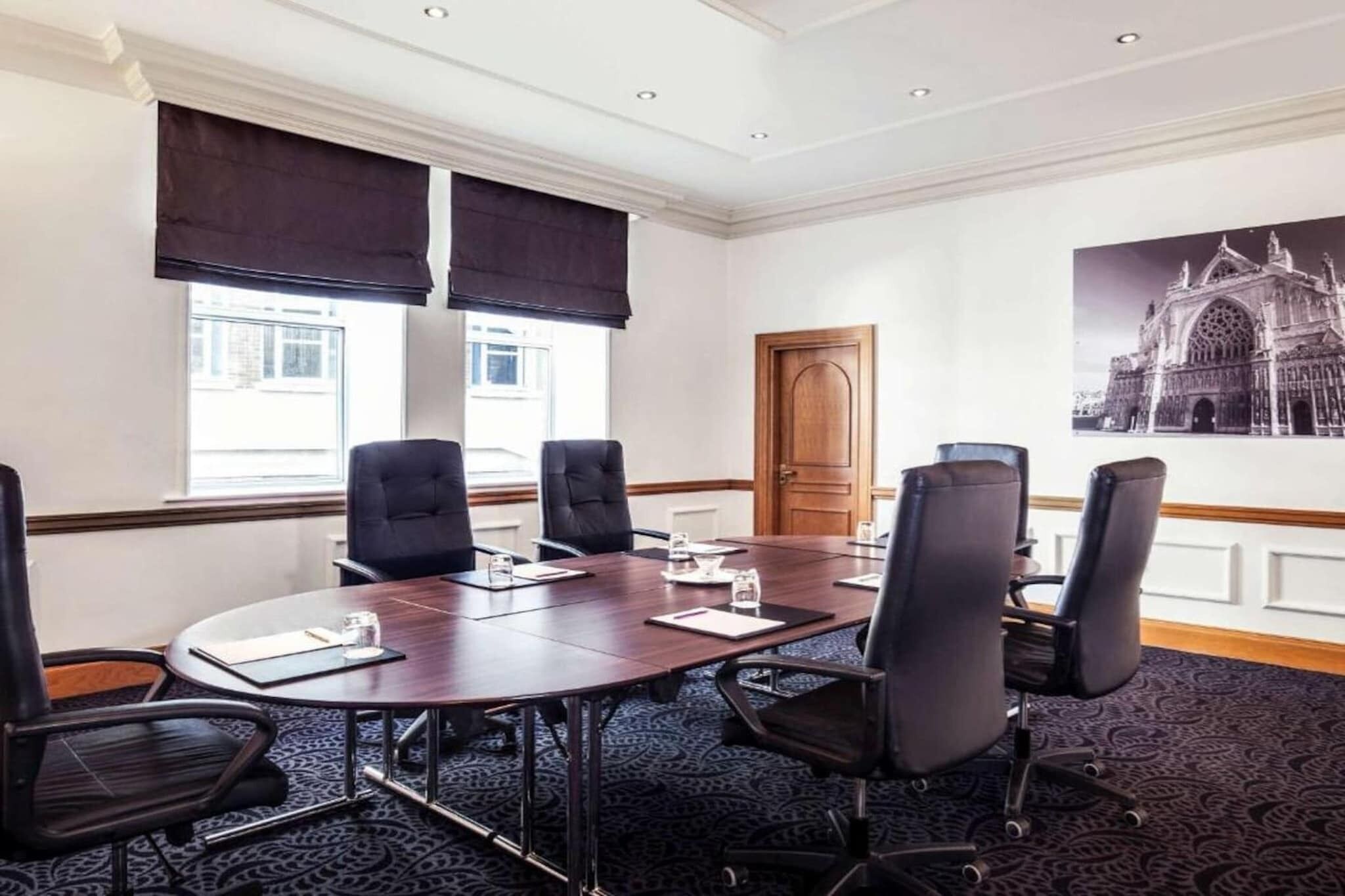 A conference room with a large table, black chairs, and a large window with blinds.