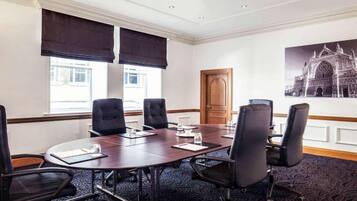 A conference room with a large table, black chairs, and a large window with blinds.