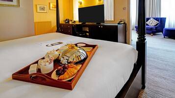 A hotel room with a neatly made bed, a tray with breakfast items, a desk with a computer, and a TV.