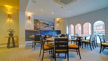 A dining area with round tables and chairs, a mural on the wall, and large windows with a view of buildings.