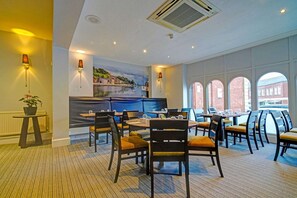 A dining area with round tables and chairs, a mural on the wall, and large windows with a view of buildings. - Exeter Rougemont by Sunday - Privilege King Room (Exeter)