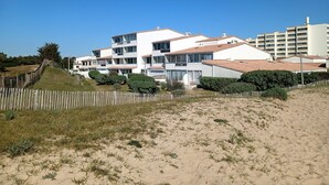A coastal residential area with modern white buildings, a sandy beach, and a wooden fence.