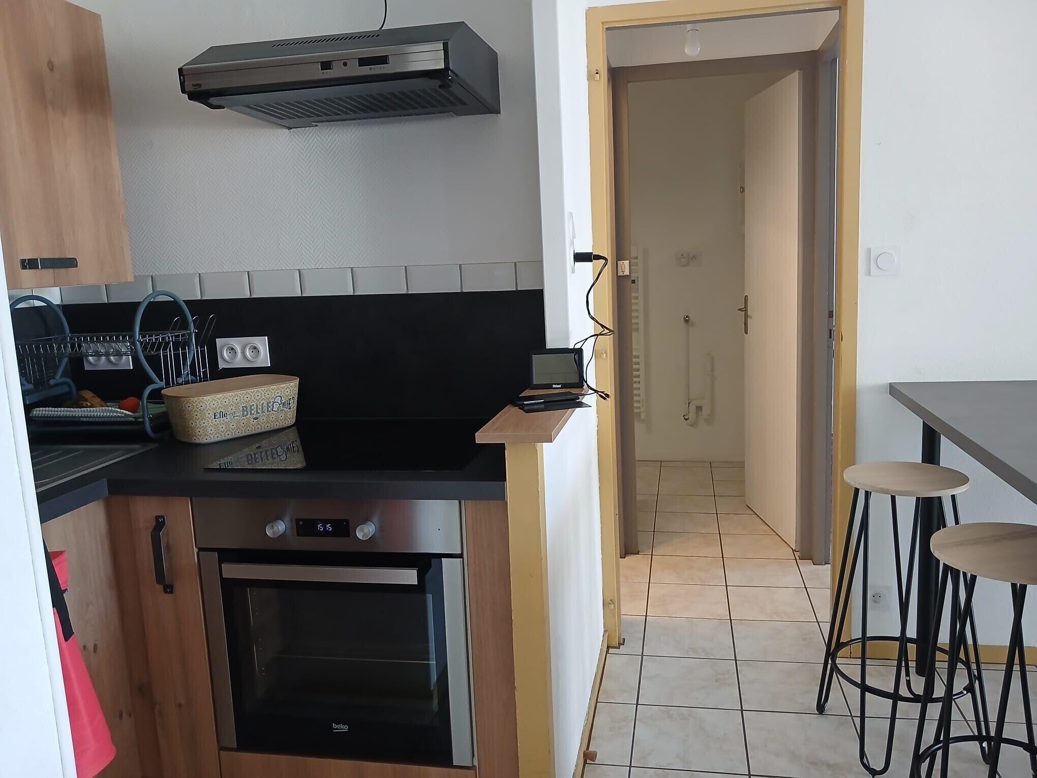 A kitchen with a built-in oven, a microwave, and a coffee machine. There is a small dining area with a table and two stools.