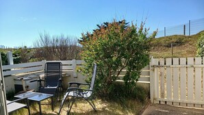 A patio with two chairs and a table, surrounded by a white fence and vegetation.